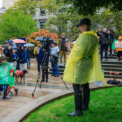 A woman in a bright translucent poncho in the rain, with a crowd of people and a camera watching.
