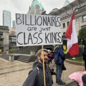 A man in front of the Hotel Vancouver and Art Gallery with a big sign and a Canadian flag.