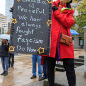 An a grandmother in a bright red coat with a sign reading: Canada is peaceful... We always fought fascism and do now.