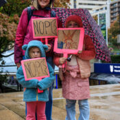A smiling mother and her two shy kids dressed in pink holding to signs reading 'Nope' and one saying 'No Kings'