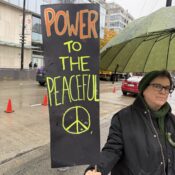 A woman under a wet umbrella with a sign reading: 'Power to the Peaceful'