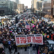 From the air, a packed crowd filling a six lane city road into the far distance, wearing winter clothing and carrying anti-ice signs, including one that reads "Minnesota General Strike: the people have the power to stop ice terror